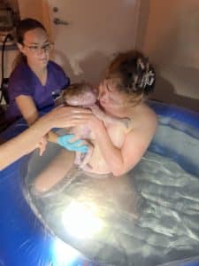Mother cradling newborn in birthing pool after home water birth