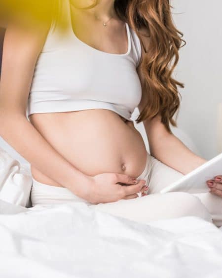 Pregnant mother on a bed looking at computer tablet