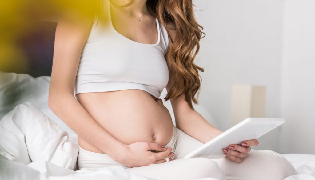 Pregnant mother with tablet and holding belly