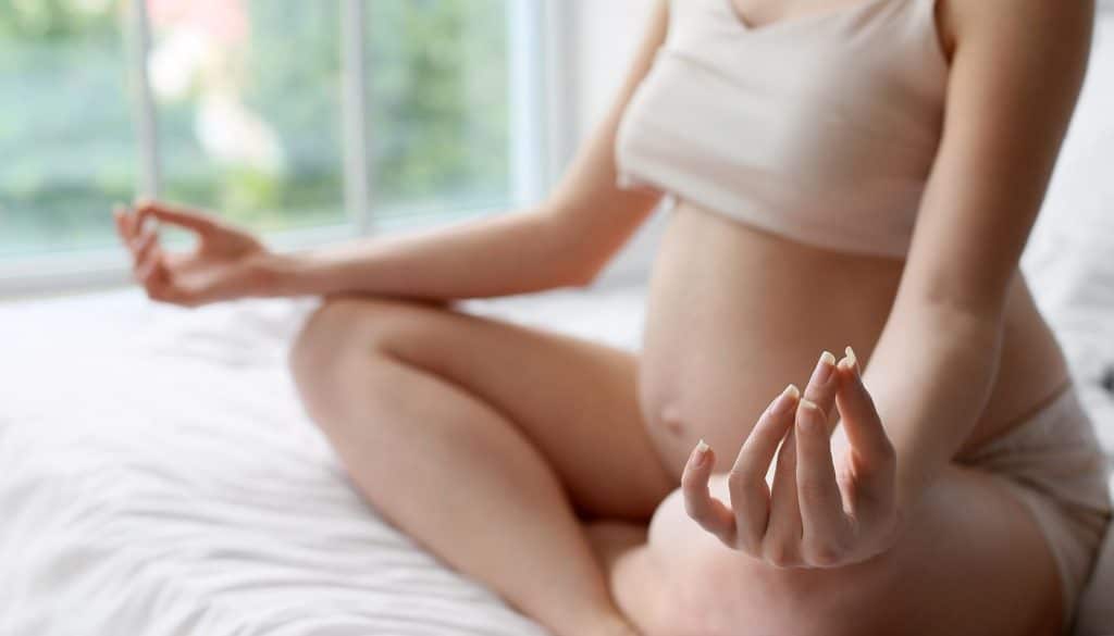 Young pregnant woman meditating on bed at home