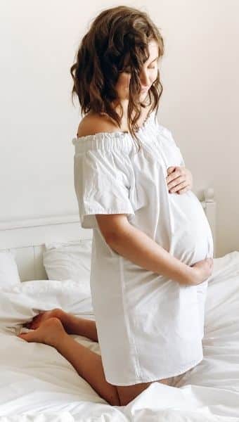 Pregnant mother in long white dress holding belly