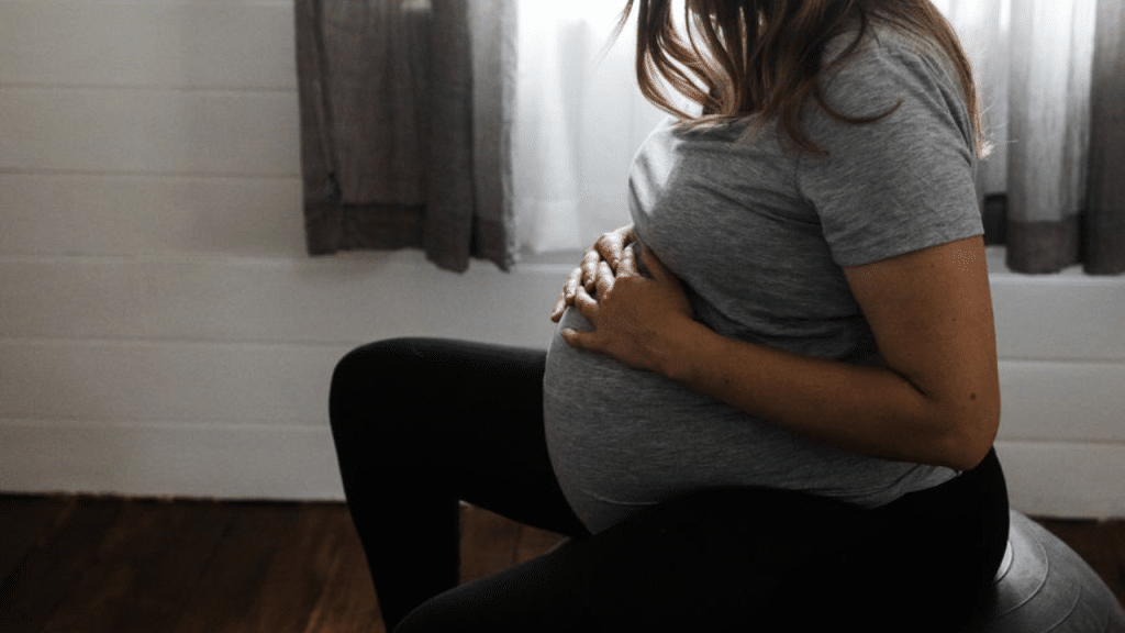Hypnobirthing mother holding belly sitting on a birth ball.
